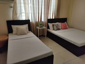 A room with two beds, a small table with a plant, and a window with curtains. - Fiesta Ballroom Hotel (Legazpi)