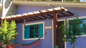 Uma casa com pergolado de madeira, uma rede e um jardim com flores e arbustos.