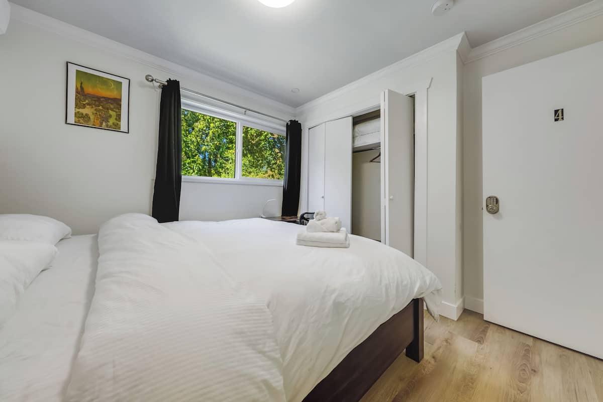 A bedroom with a large bed, a window with curtains, a wardrobe, and a door.