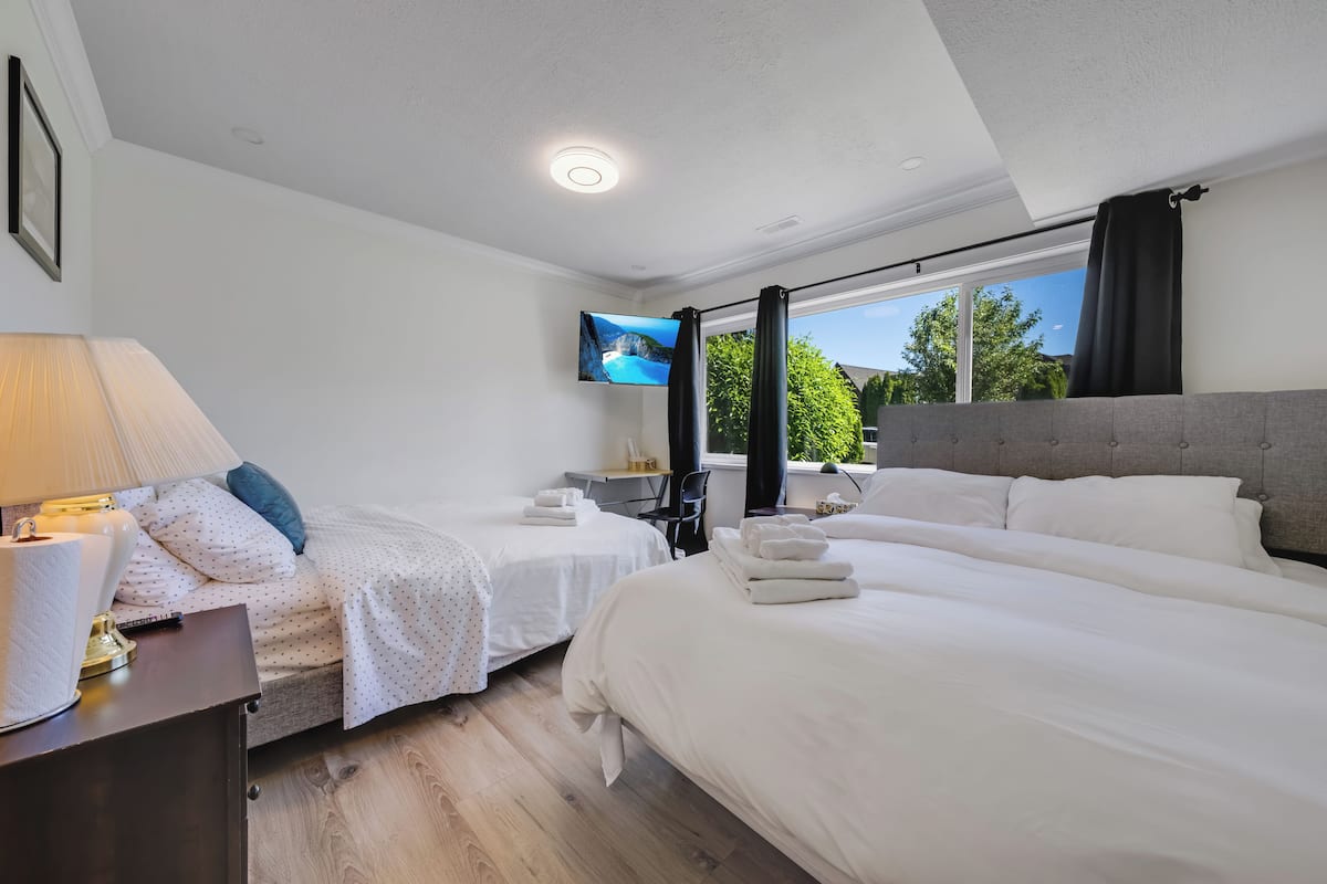 Ein Hotelzimmer mit zwei Betten, einem Fernseher, einem Schreibtisch mit Lampe und einem Fenster mit Vorhängen.