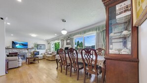 Een ruime woonkamer met een houten eettafel en stoelen, een televisie en een open haard.