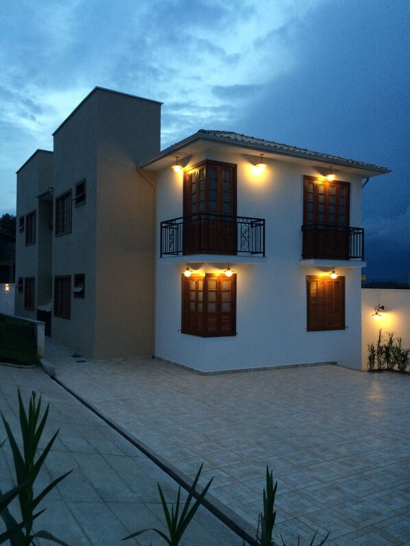 A modern two-story building with a flat roof, multiple balconies, and exterior lighting.