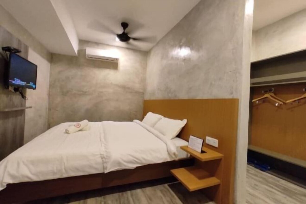 Une chambre d’hôtel avec un lit, un téléviseur fixé au mur, un ventilateur de plafond et une armoire en bois.