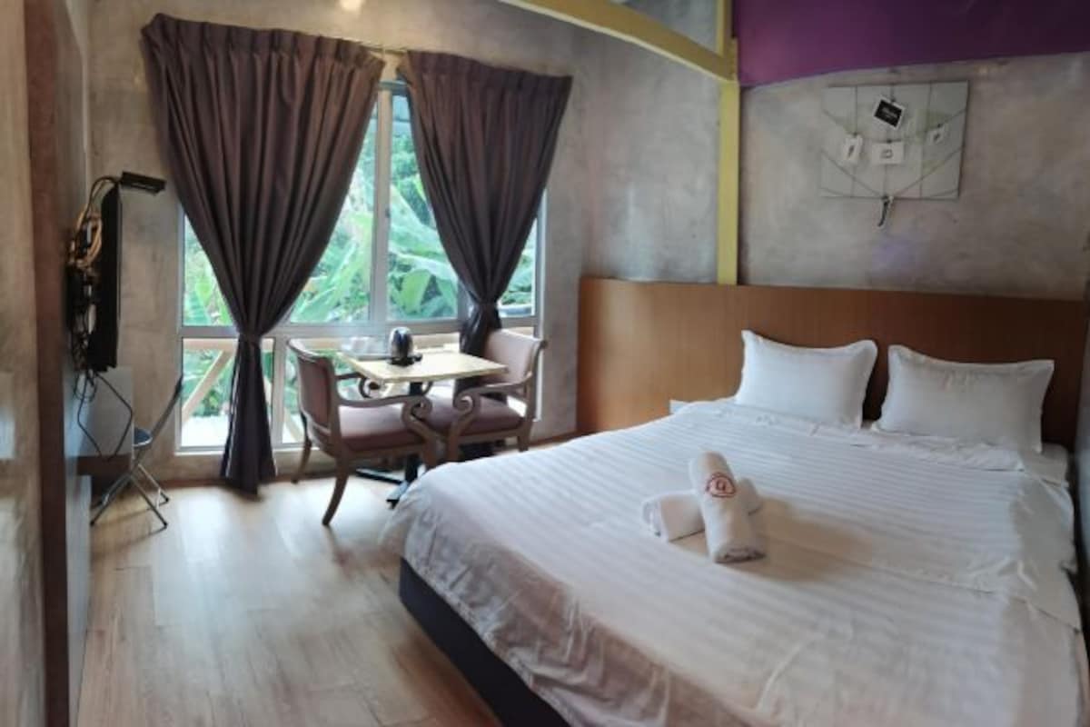 Habitación de hotel con cama, escritorio y silla. Se ve una ventana con cortinas, e interruptor de luz en la pared.