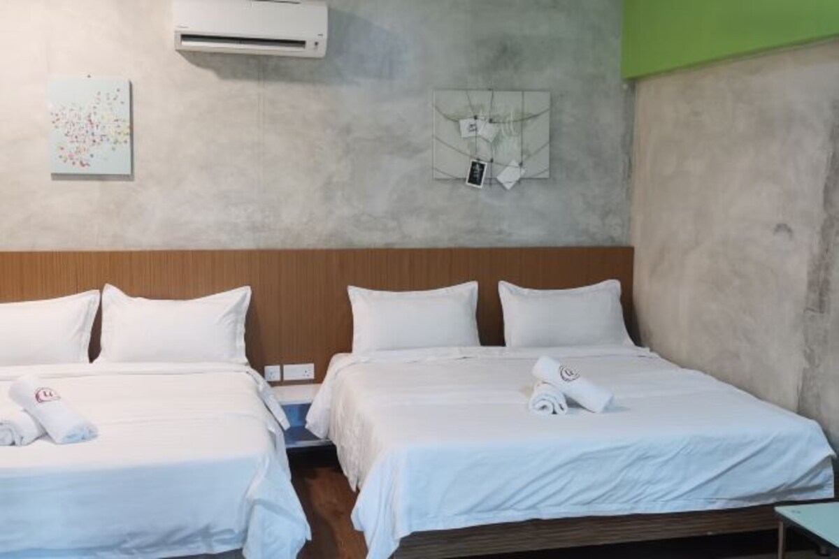 Ein Hotelzimmer mit zwei Betten, weißer Bettwäsche, einem Holz-Kopfteil, einer Klimaanlage und einer Wandleuchte.