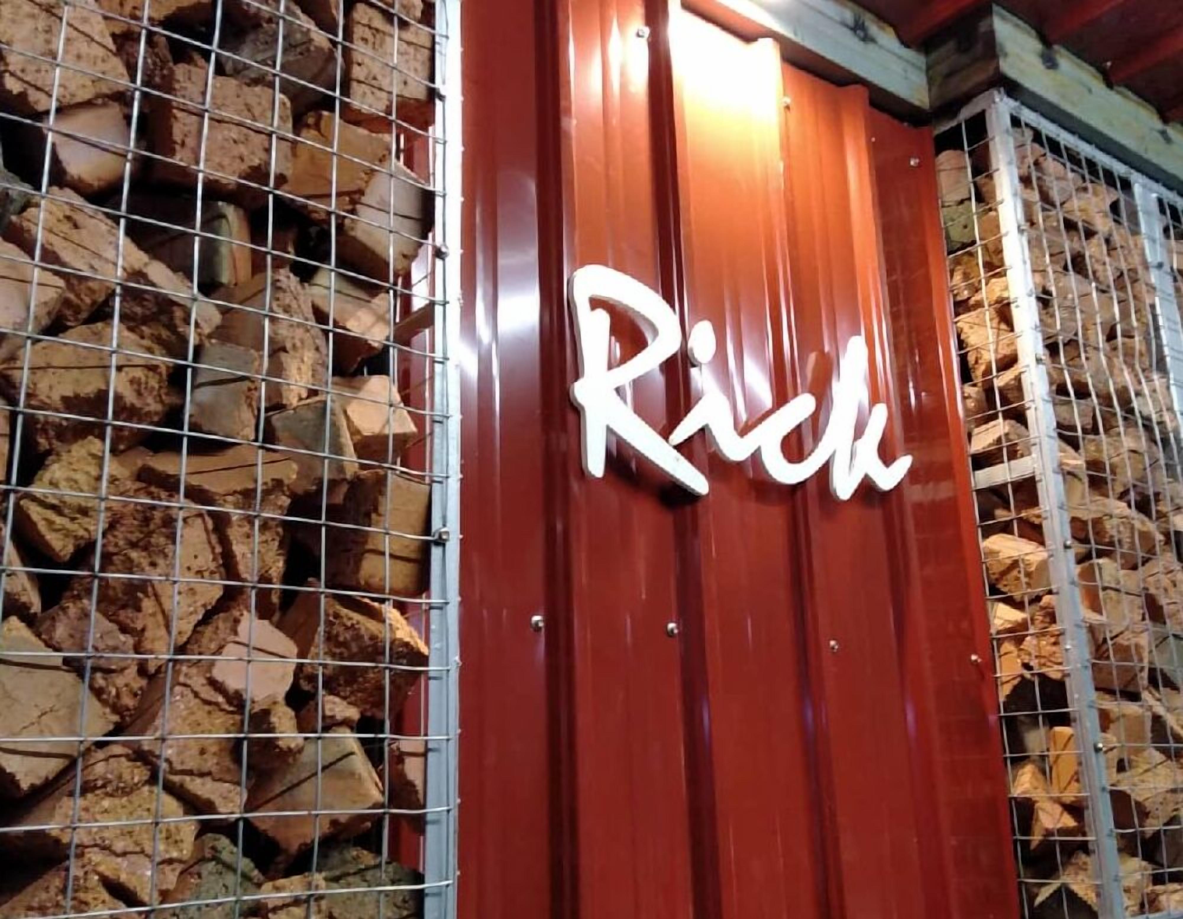 A sign with the word "Rice" in a stylized font, mounted on a red wall with a metal grid structure behind it.