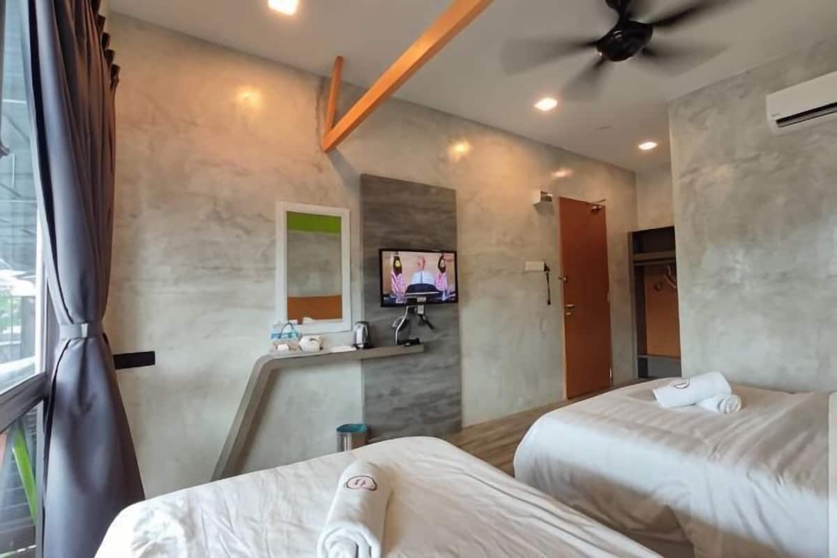 A hotel room with two beds, a TV on the wall, a ceiling fan, and a bathroom with a shower and toilet.