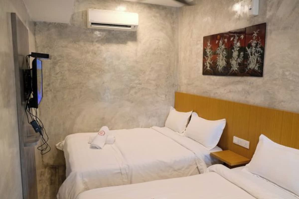 Habitación de hotel con dos camas, un equipo de aire acondicionado, un cuadro en la pared y un televisor montado en la pared.