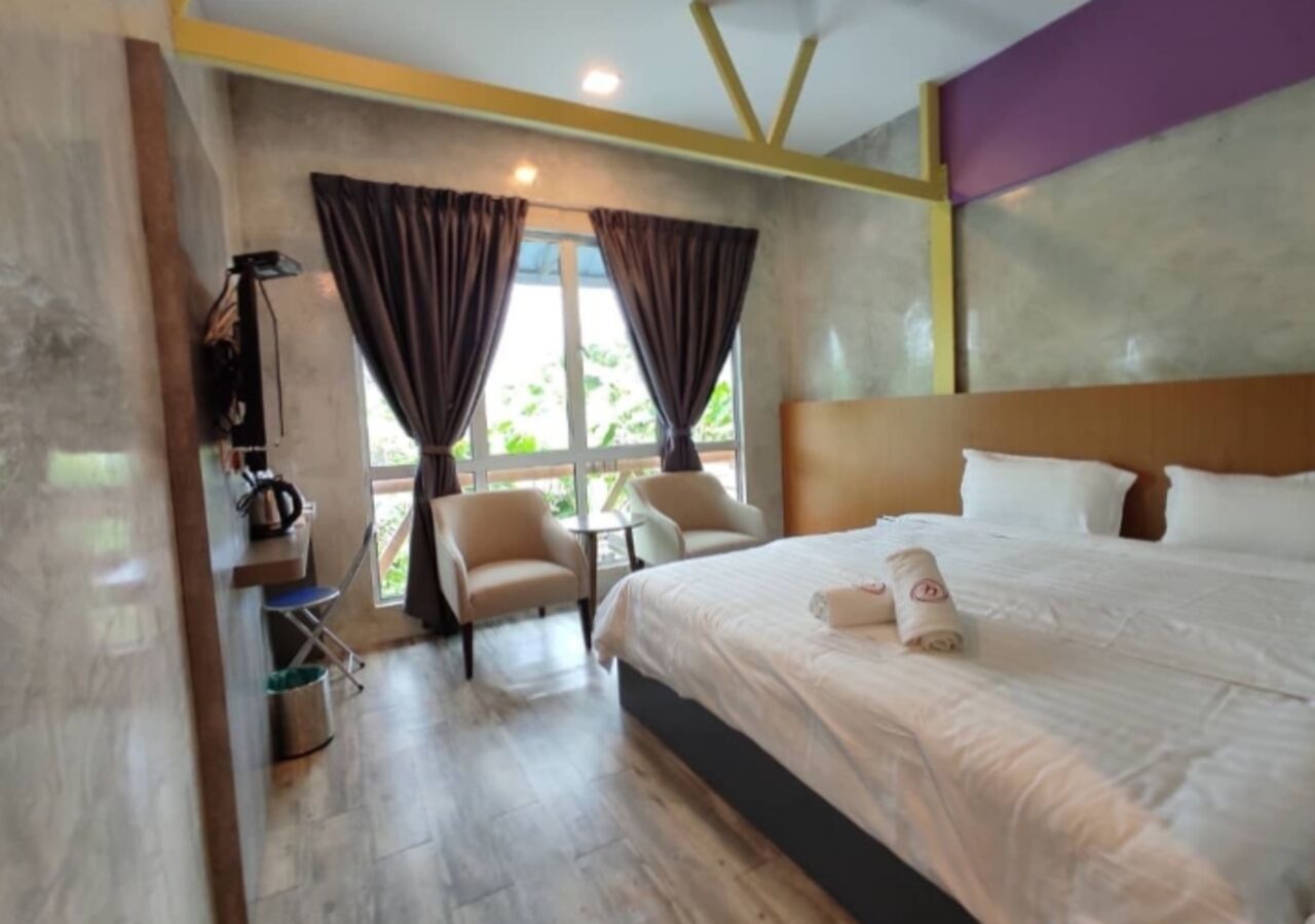 A hotel room with a bed, two chairs, a small table, a coffee maker, and a window with curtains.