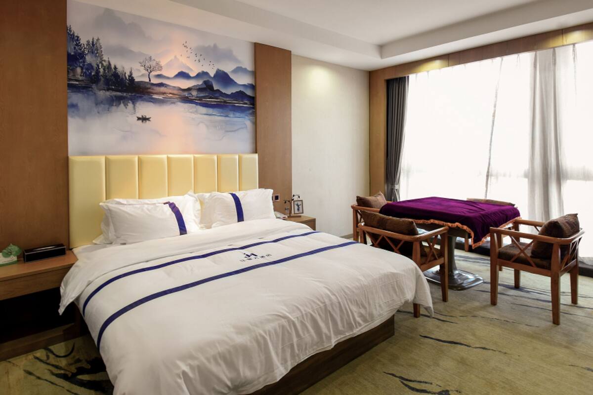 Een hotelkamer met een groot bed, een bureau met stoel, een schilderij aan de muur en uitzicht op het groen.