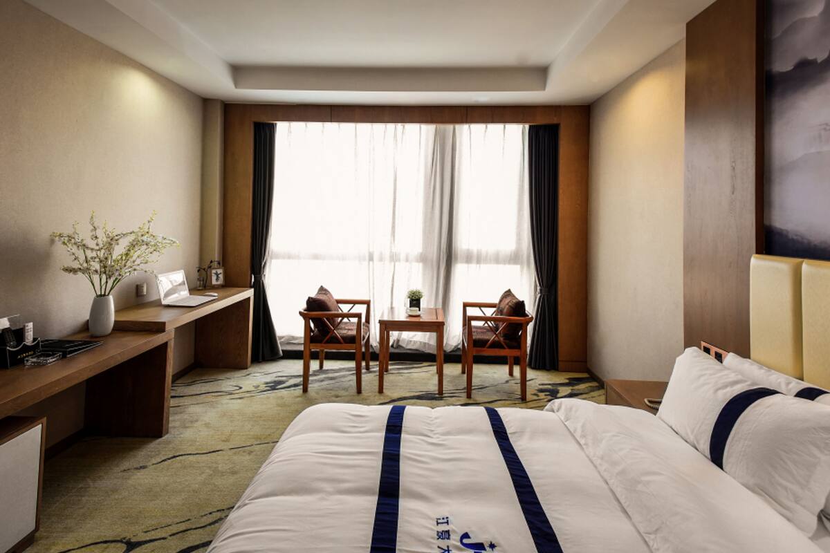 Hotelkamer met een groot bed, een bureau, twee stoelen, een bijzettafeltje en een raam met gordijnen.