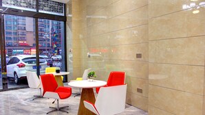 A modern indoor seating area with a round table and red and white chairs, a small plant, and a view of the street through large windows. - Guiyang Jianghao Grand Hotel (Guiyang)