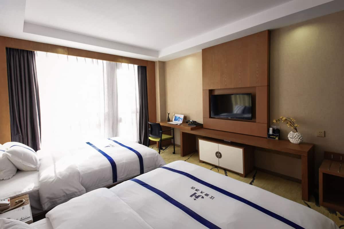 Een hotelkamer met twee bedden, een bureau, een televisie en een klein kastje.