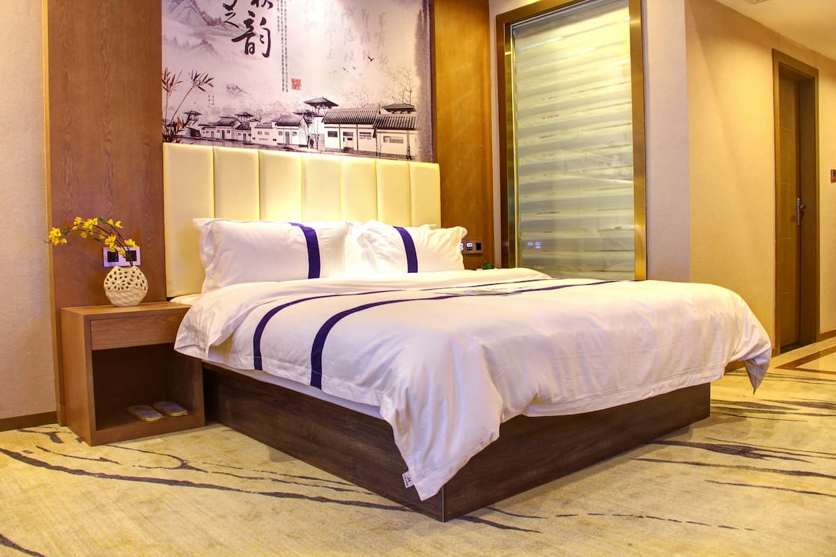 Een hotelkamer met een groot bed, een nachtkastje met een bloevas en een muur met een traditionele muurschildering.