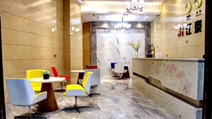 A lobby with a reception desk, seating area with chairs, and a marble wall. - Guiyang Jianghao Grand Hotel (Guiyang)