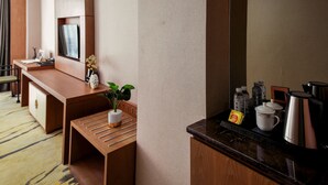 A hotel room with a wooden desk, a small table with a plant, a TV mounted on the wall, and a coffee station with a kettle and cups. - Guiyang Jianghao Grand Hotel (Guiyang)