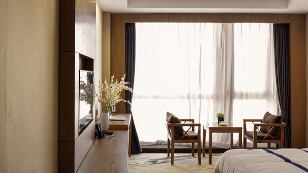 A hotel room with a bed, two chairs, a small table, a TV, and a window with curtains. - Guiyang Jianghao Grand Hotel (Guiyang)