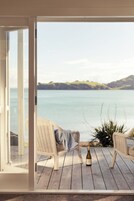 Un balcone con sedie in vimini, una bottiglia di vino e vista su un lago tranquillo e dolci colline in lontananza.