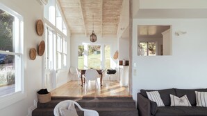 A spacious living area with a dark-colored sofa, a white chair, and a dining table with chairs. - Circular Bay (Waiheke Island)