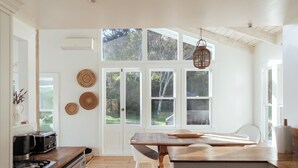 A kitchen with a wooden countertop, white cabinets, a dining table, and large windows. - Circular Bay (Waiheke Island)