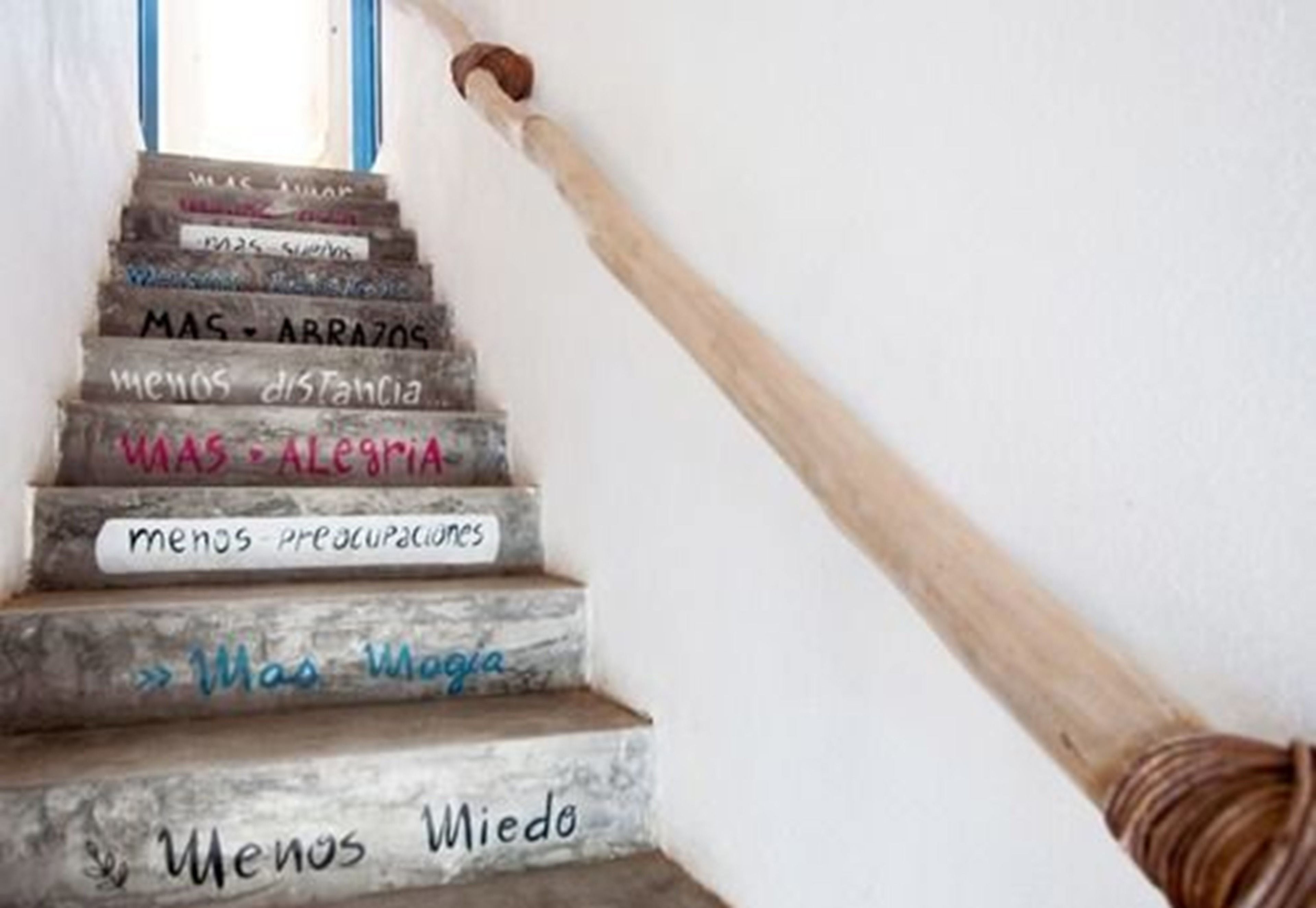 Una escalera de madera con peldaños que exhiben frases como “MÁS – AMOR” y “MENOS – Miedo”.