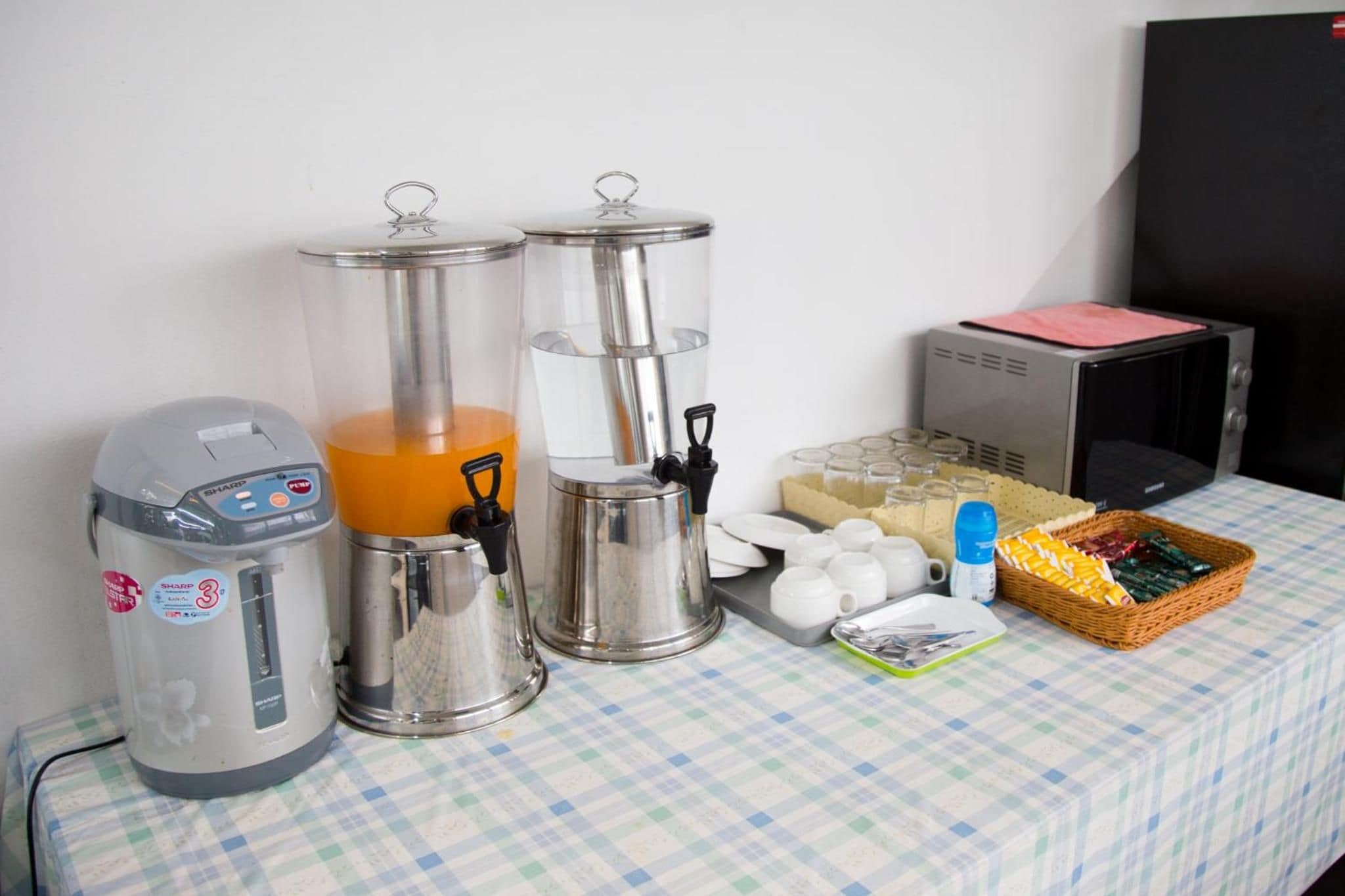 Un área de cocina con cafetera, dos dispensadores de café, microondas y una cesta de bocadillos.