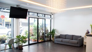 A modern interior with a grey sofa, a TV mounted on the wall, and a large window with a view of the outside. - Moca Hotel (Bangkok)