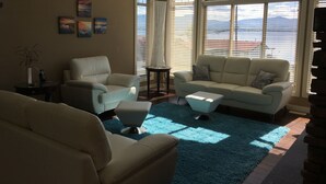 Een woonkamer met een groot raam, een blauw vloerkleed en een beige bank.