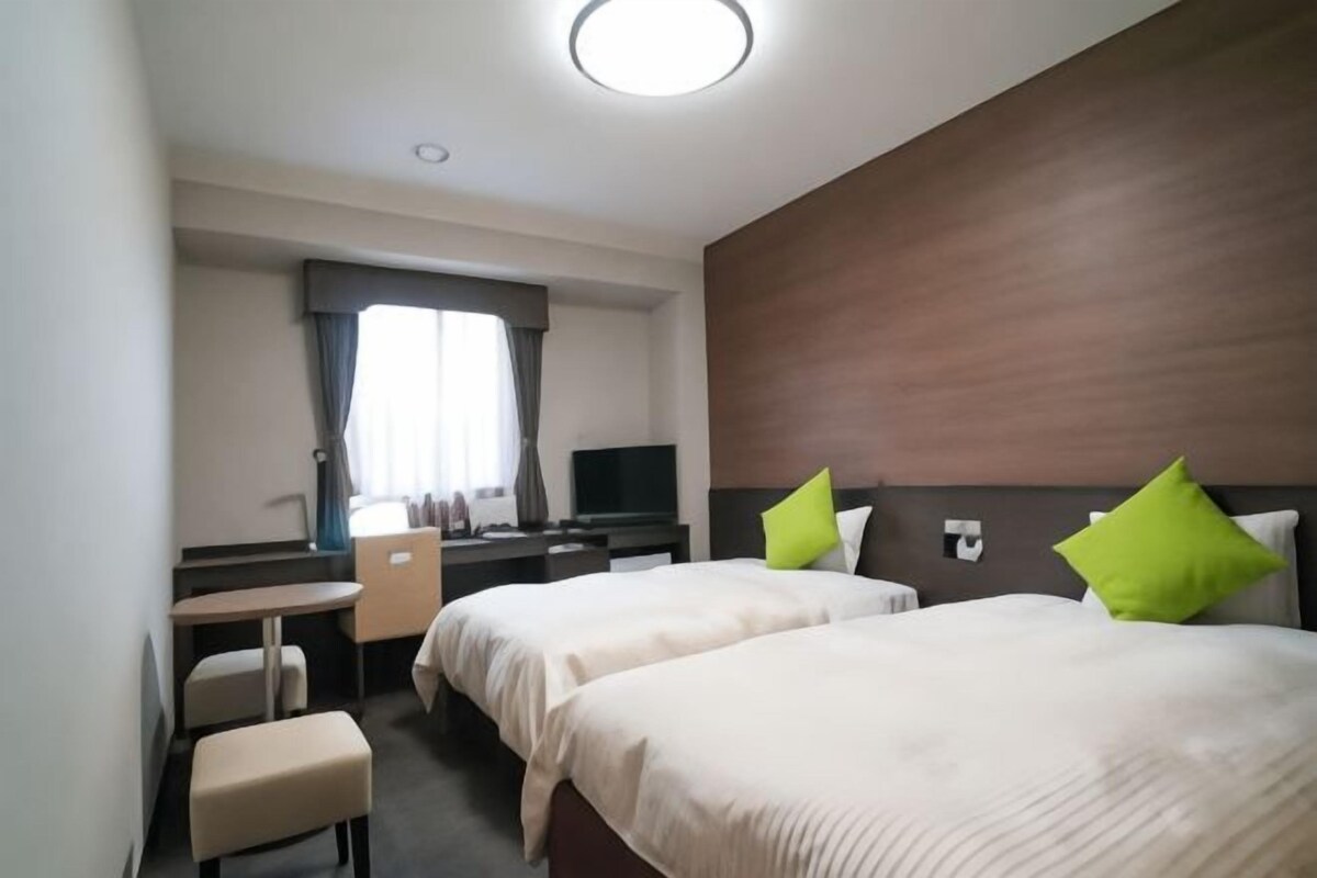 Habitación de hotel con dos camas, un escritorio, una silla, un televisor y una ventana con cortinas.