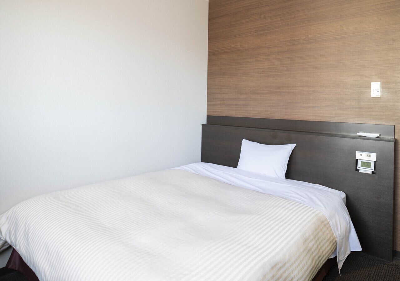 Una habitación de hotel con una cama individual, cabecera de madera y panel de control en la pared.