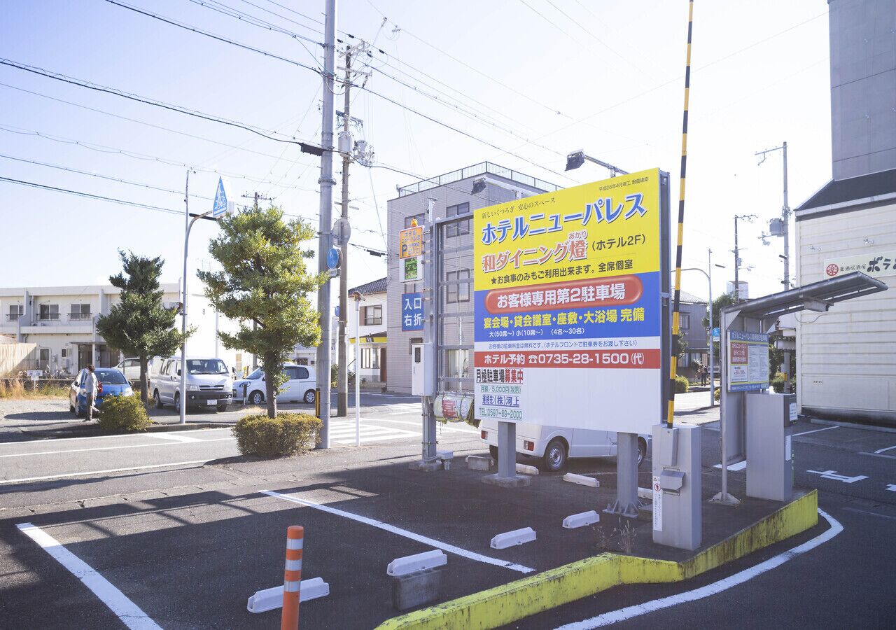 A hotel sign with Japanese text, a parking lot, and a building in the background.