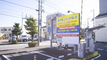 A hotel sign with Japanese text, a parking lot, and a building in the background.