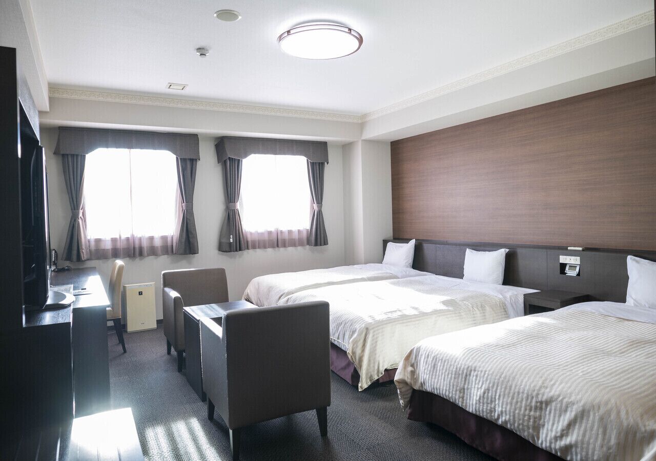 Ein Hotelzimmer mit zwei Betten, einem Schreibtisch, einem Stuhl und einem Fernseher.