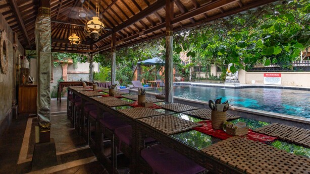 An outdoor dining area with a pool view, covered by a wooden roof, and furnished with tables and chairs. - Ubud Aura Retreat (Ubud)