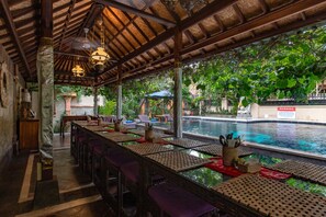 An outdoor dining area with a pool view, covered by a wooden roof, and furnished with tables and chairs. - Ubud Aura Retreat (Ubud)