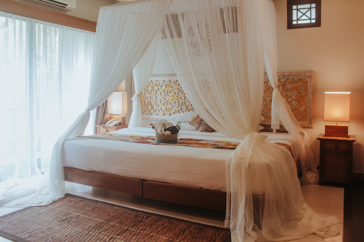 A bedroom with a four-poster canopy bed, a bedside table with a lamp, and a decorative headboard.