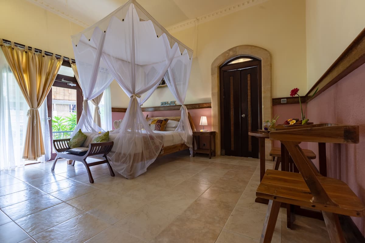 A bedroom with a bed under a canopy, a wooden bench, a nightstand, and a view of the outdoors.