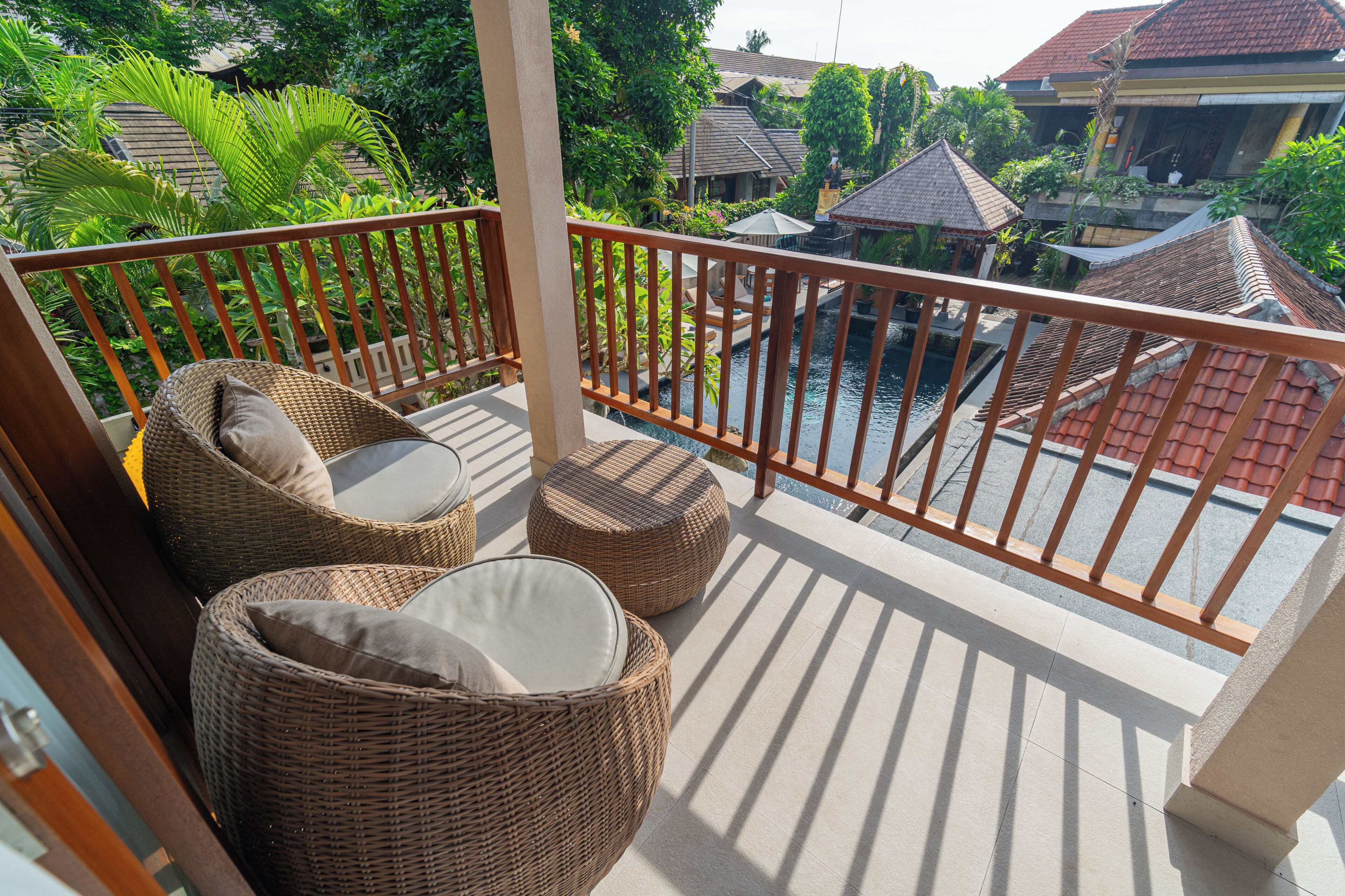 A balcony with wicker furniture, a pool, and a view of a traditional house.