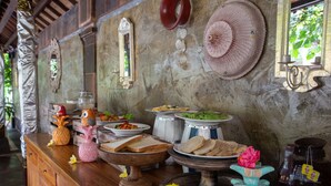 A wooden buffet table with various dishes, a decorative mirror, and a rustic stone wall. - Ubud Aura Retreat (Ubud)