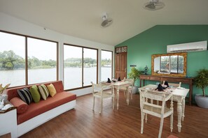 Un espacio amplio con ventanas grandes que dan a una masa de agua, una zona de comedor con mesa y sillas, y un sofá con cojines.