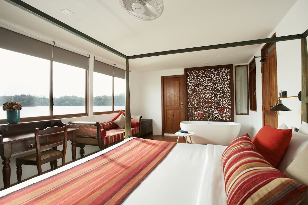 A bedroom with a large bed, a desk, a chair, a bathtub, and a view of the outdoors.