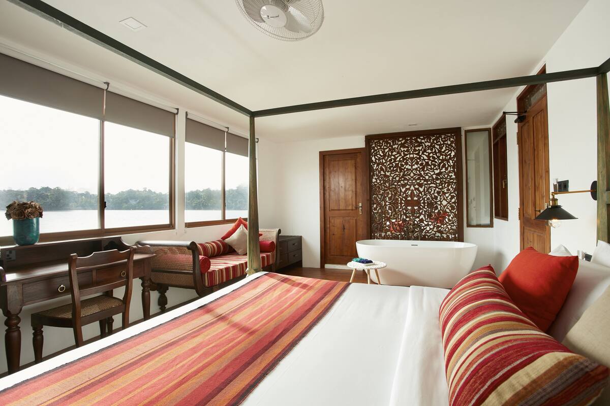 A bedroom with a large bed, a desk, a chair, a bathtub, and a view of the outdoors.