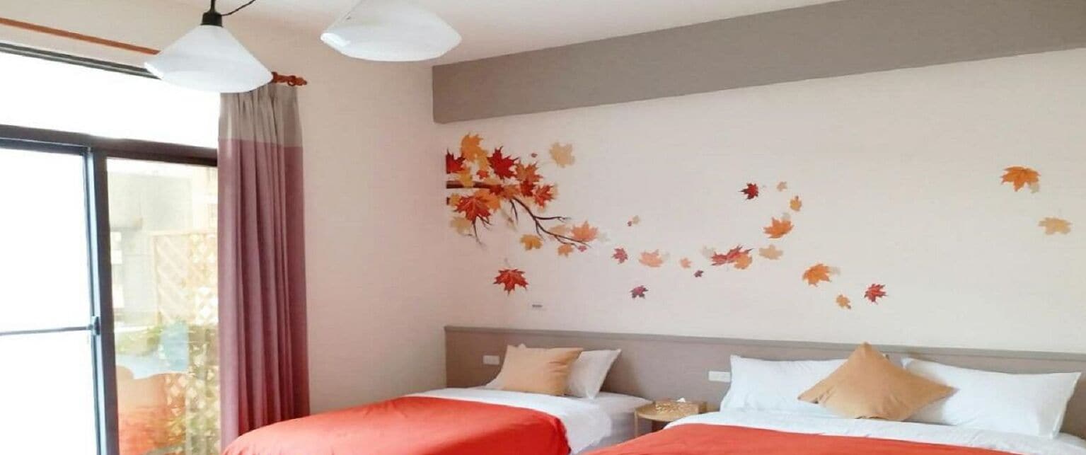 Une chambre d’hôtel avec deux lits, une grande fenêtre avec des rideaux et un mur décoré de feuilles d’automne.