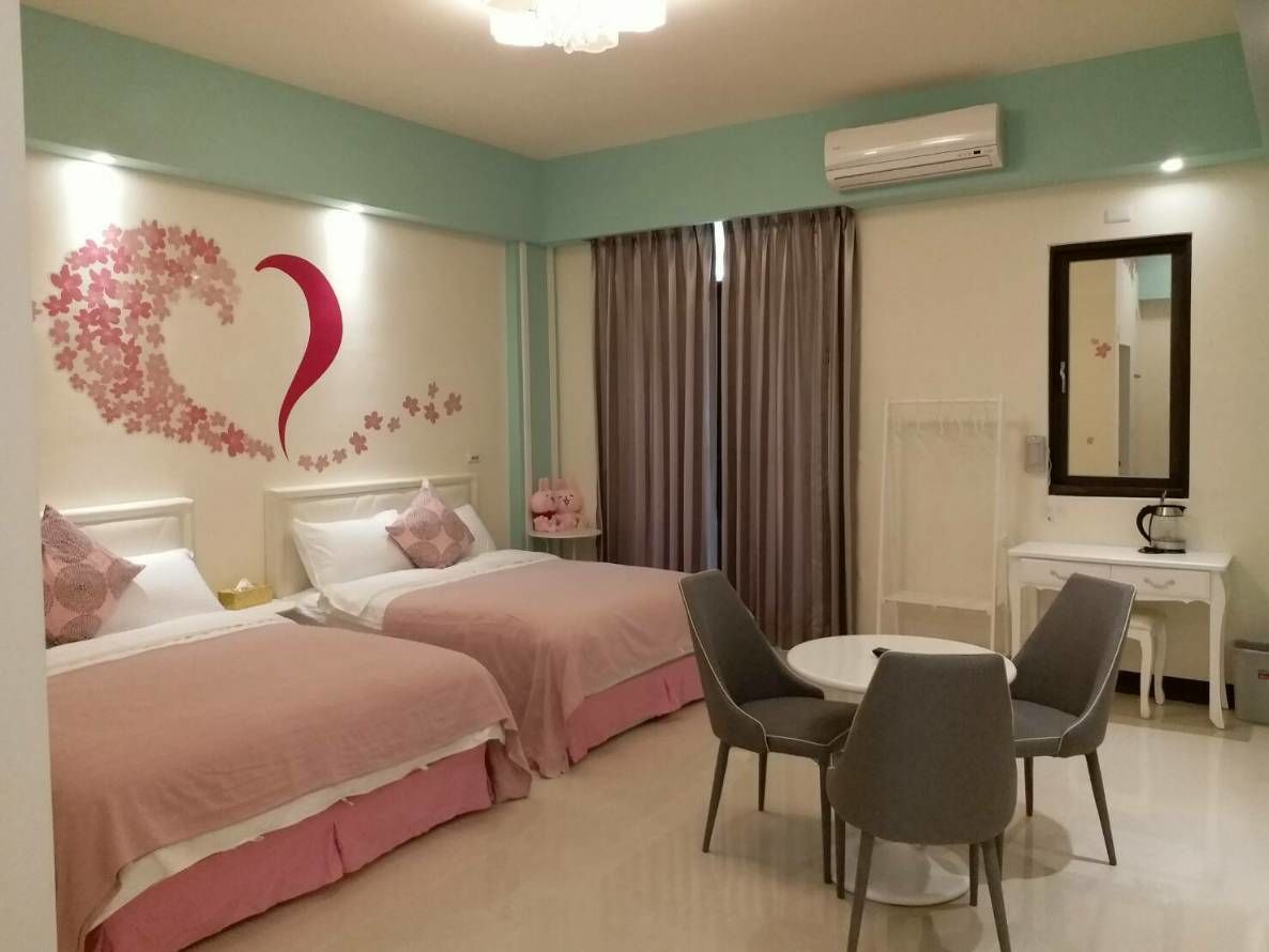 A hotel room with two beds, a desk, a chair, and a round table.