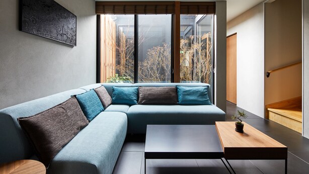 A modern living room with a sectional sofa, a wooden coffee table, and a view of the outdoors through large windows.