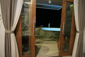 A view through a glass door leading to a swimming pool area at night. - Green Beach Inn (Penida Island)