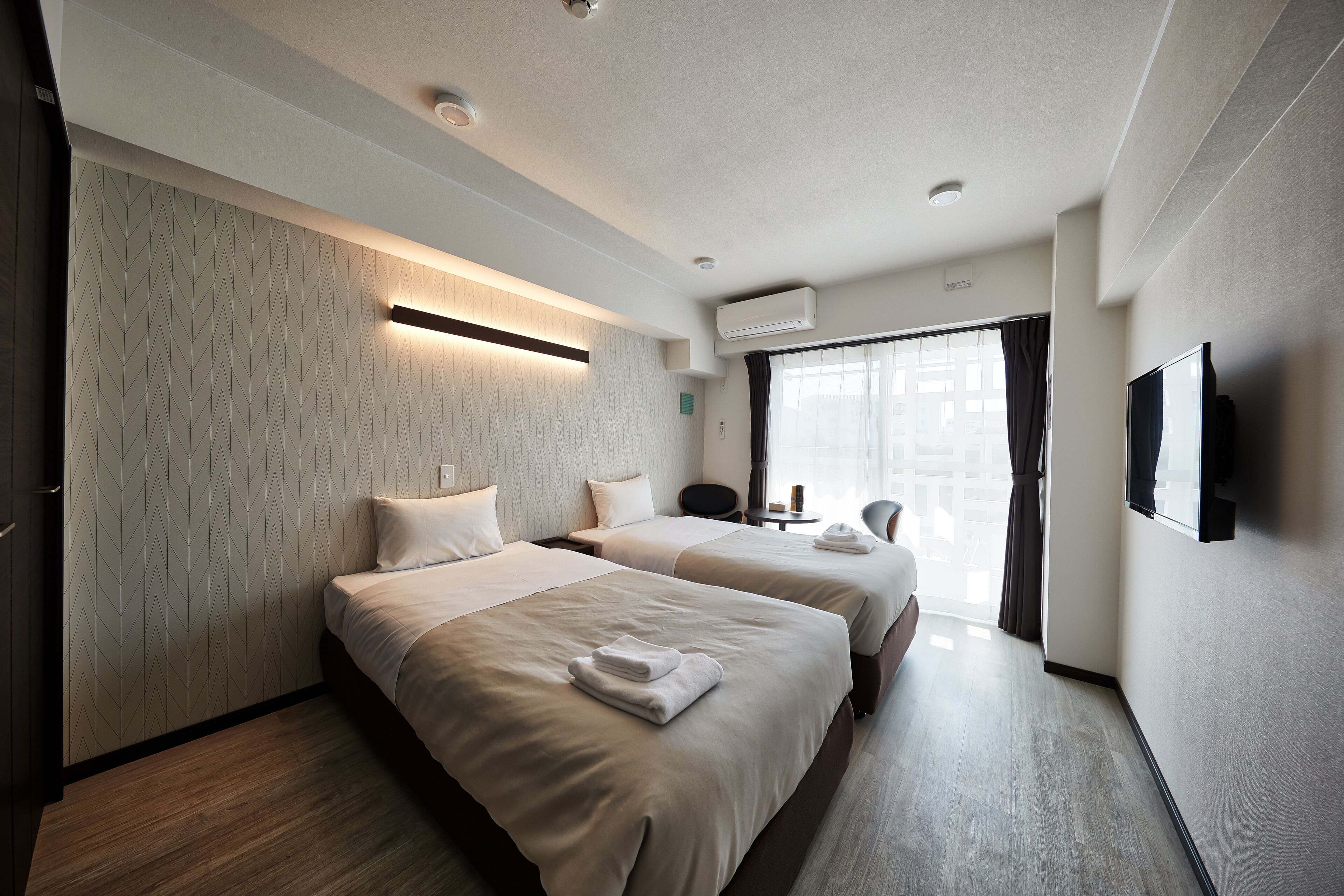 Een moderne hotelkamer met twee bedden, een flatscreen televisie en een groot raam met gordijnen.