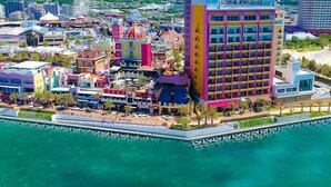 A coastal hotel with colorful buildings, a waterfront promenade, and a large building with a grid-like facade. - Arce Ryukyu Harbor Stay (Urasoe)