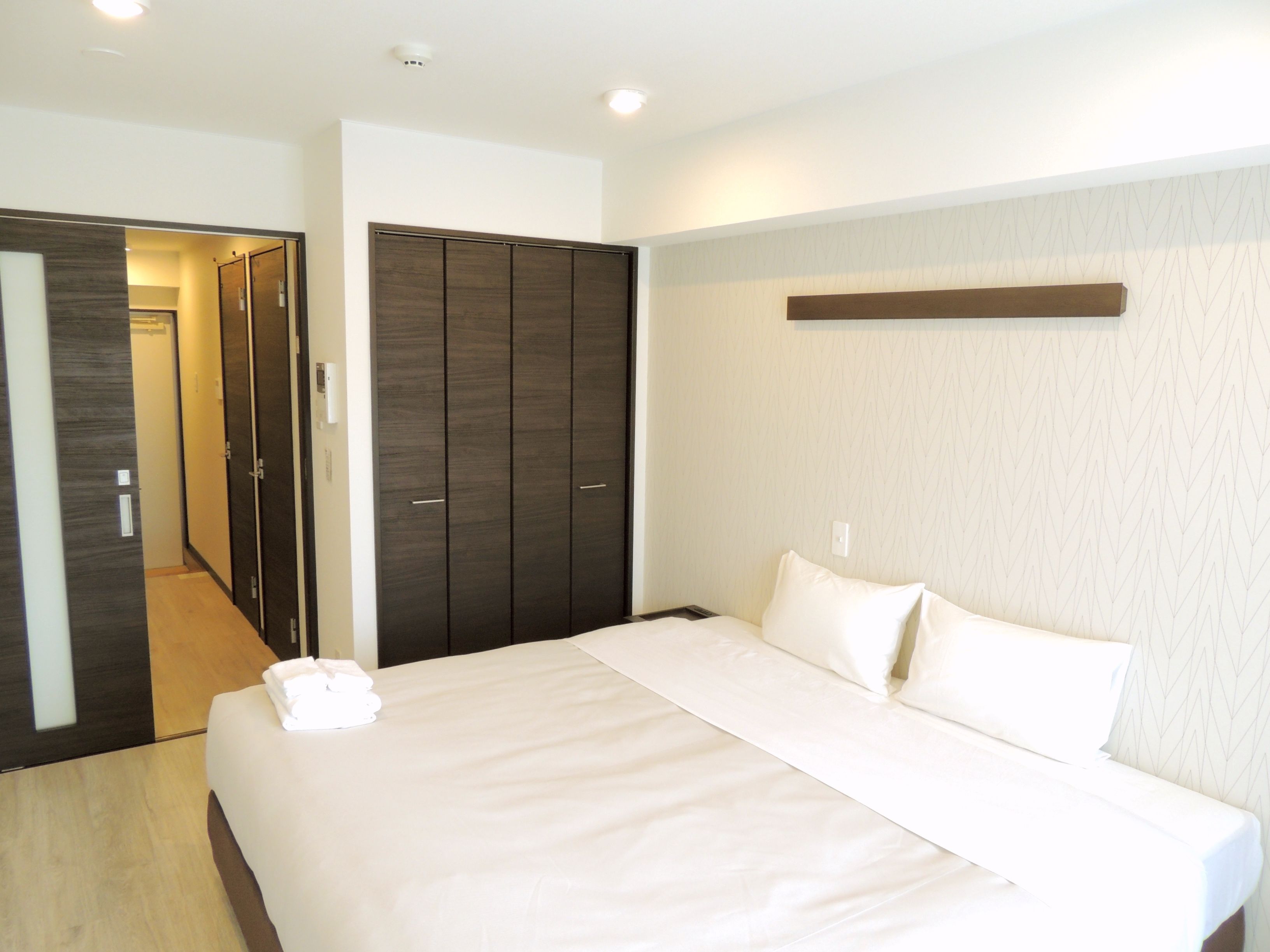 A hotel room with a large bed, dark wooden wardrobe, and a light-colored wall.