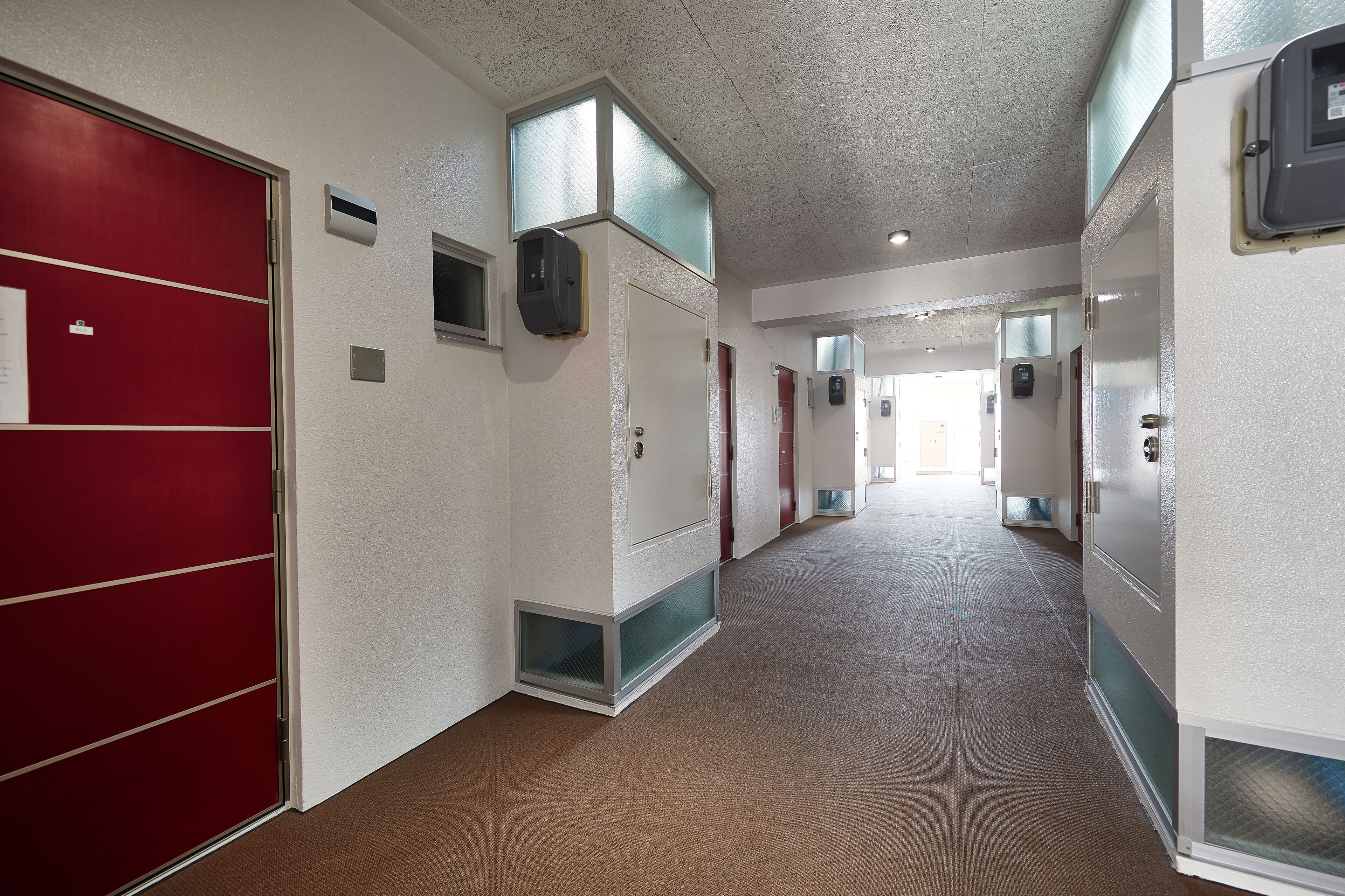 A hallway with red and white doors, air conditioning units, and a carpeted floor.